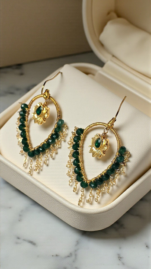 Gold and green beaded earrings on a jewelry box with a marble background