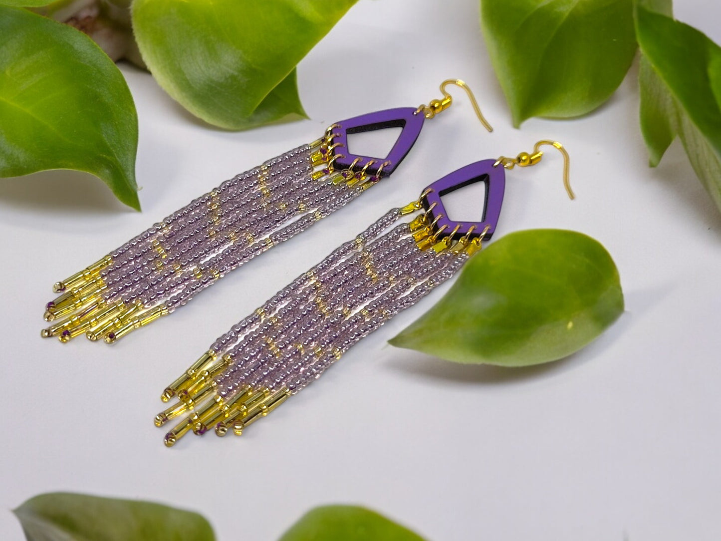 Purple and gold beaded earrings on a white surface with green leaves.