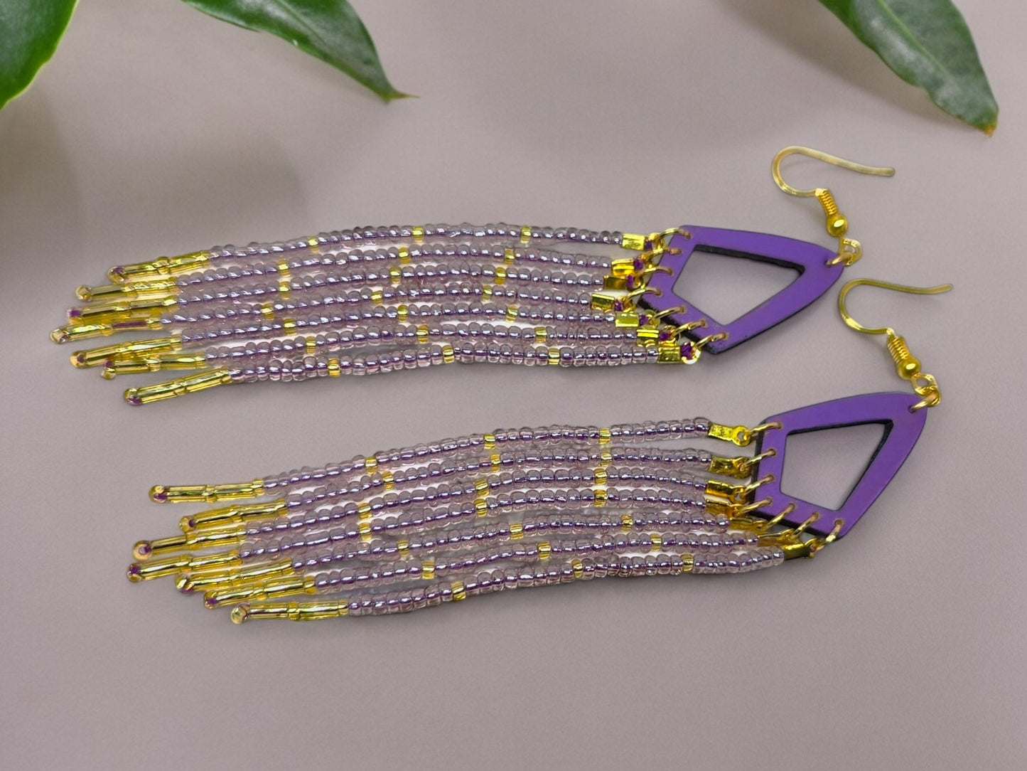 Beaded earrings with purple and gold accents on a neutral background