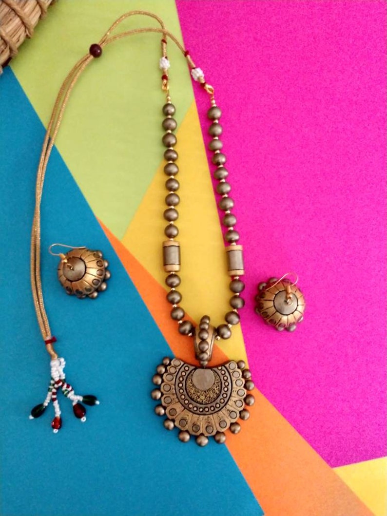 Anusangi Collections handmade terracotta jewelry set with detailed pendant and matching earrings on colorful background