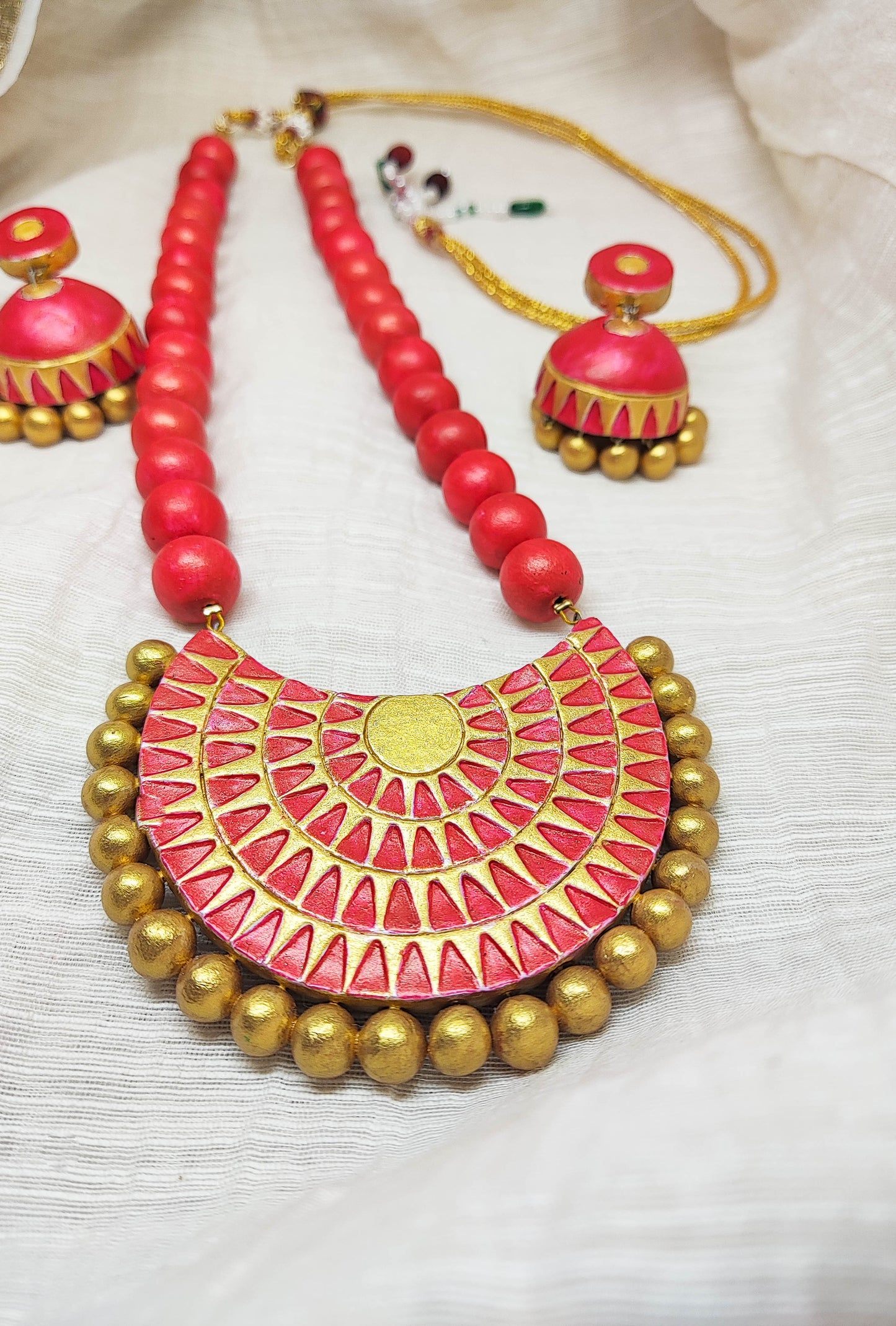 Anya terracotta jewelry set by Anusangi Collections featuring red beads and intricate gold-accented pendant with matching earrings