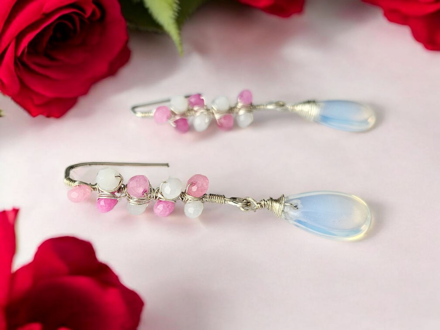 Pink and white beaded earring with blue teardrop charm from Anusangi Collections displayed with red roses
