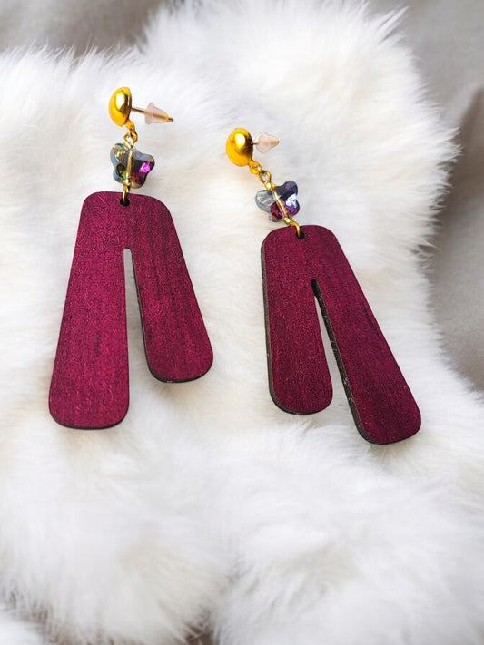 Purple wooden earrings with gold studs and small colorful butterfly charms on white fur background