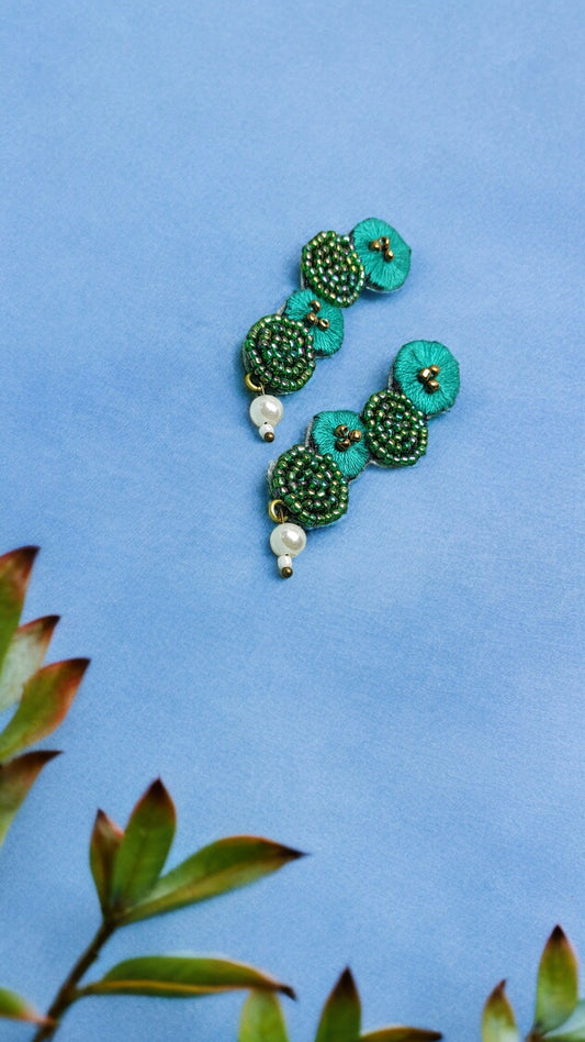 Anusangi Collections green fabric statement earrings with beadwork and pearl drops on blue background