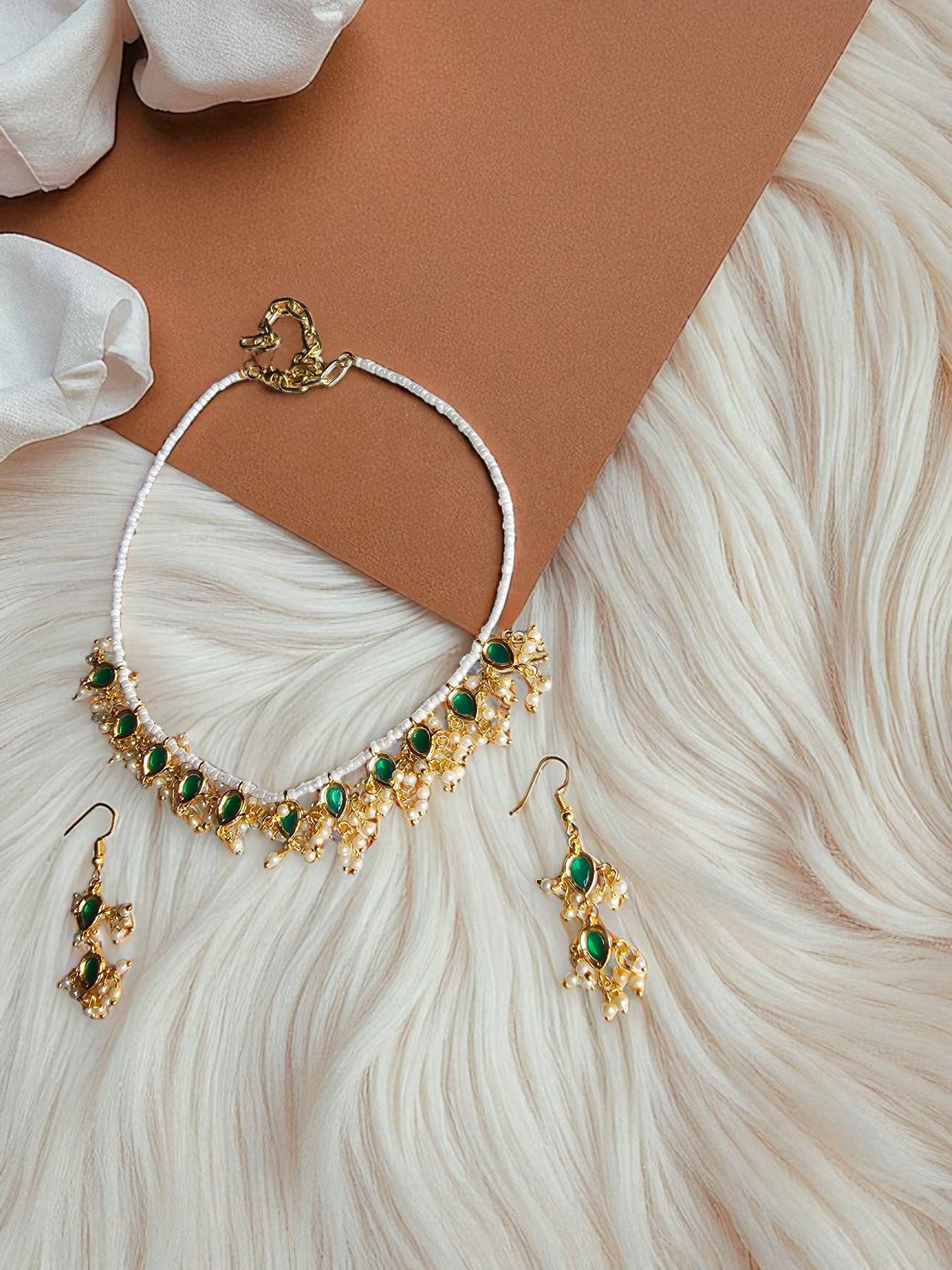 Handmade gold necklace with emerald green beads paired with matching earrings on a textured background