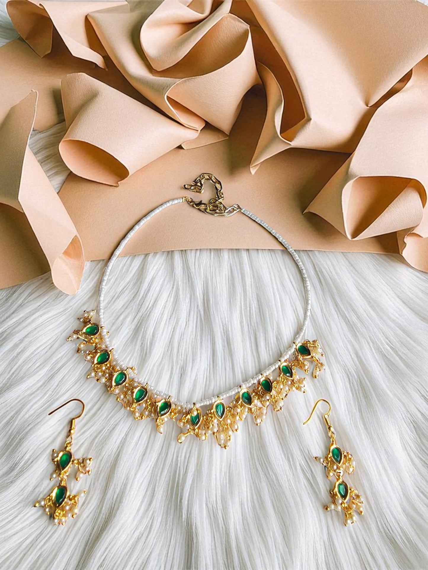 Handmade gold necklace with emerald green beads paired with matching earrings on a white fur background