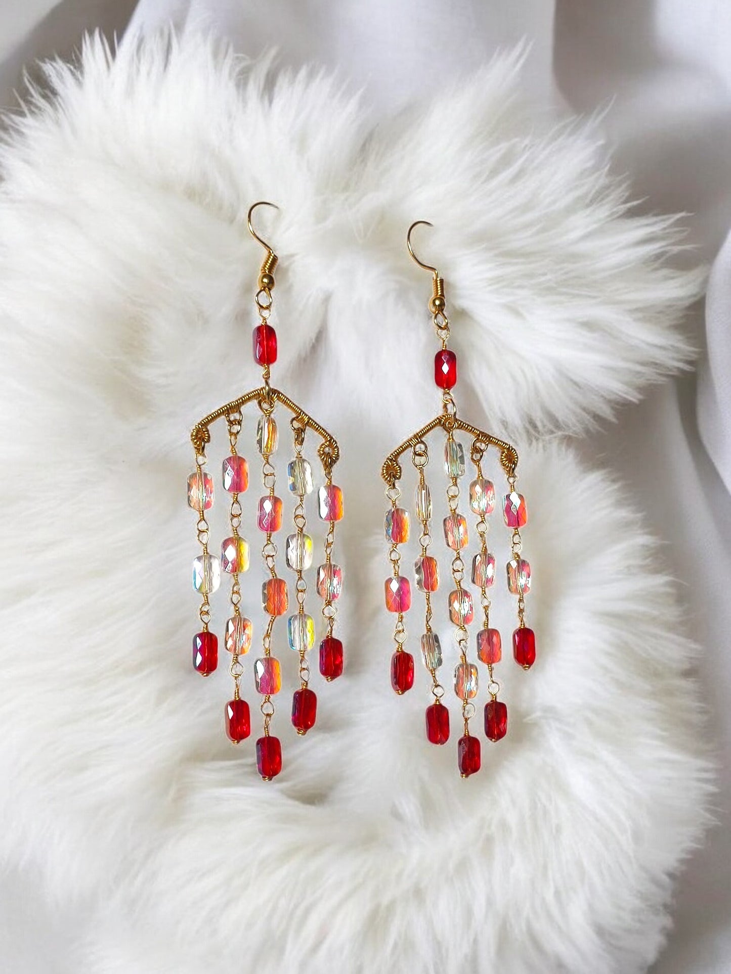 Handmade long dangle earrings with red and iridescent beads from Anusangi Collections on white fabric
