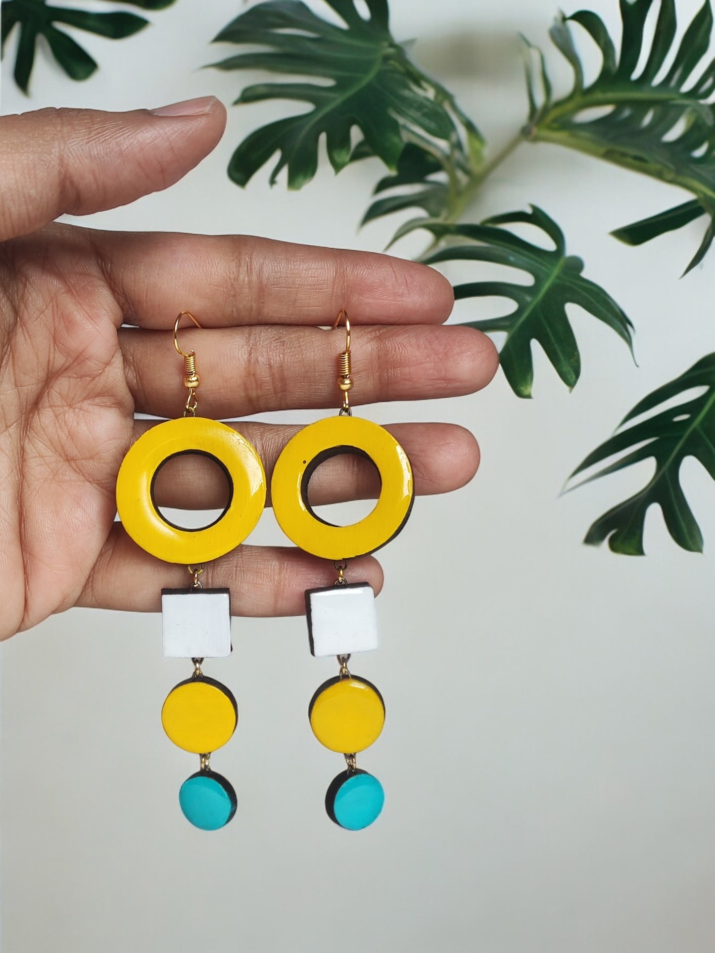 Hand holding colorful handmade terracotta earrings with yellow, white, and blue geometric shapes