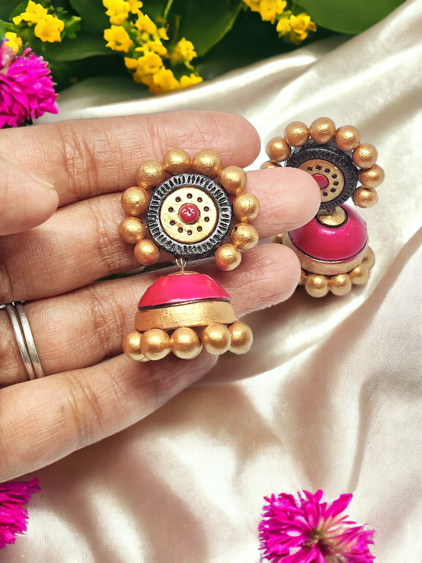 Hand holding handmade terracotta pink jhumka earrings with golden bead embellishments from Anusangi Collections