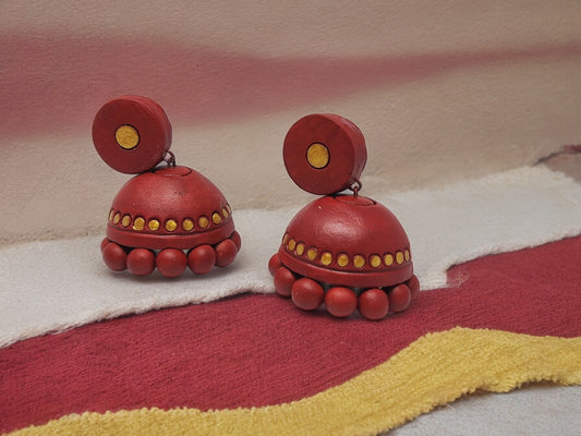 Maroon and gold terracotta earrings from Anusangi Collections displayed on fabric background