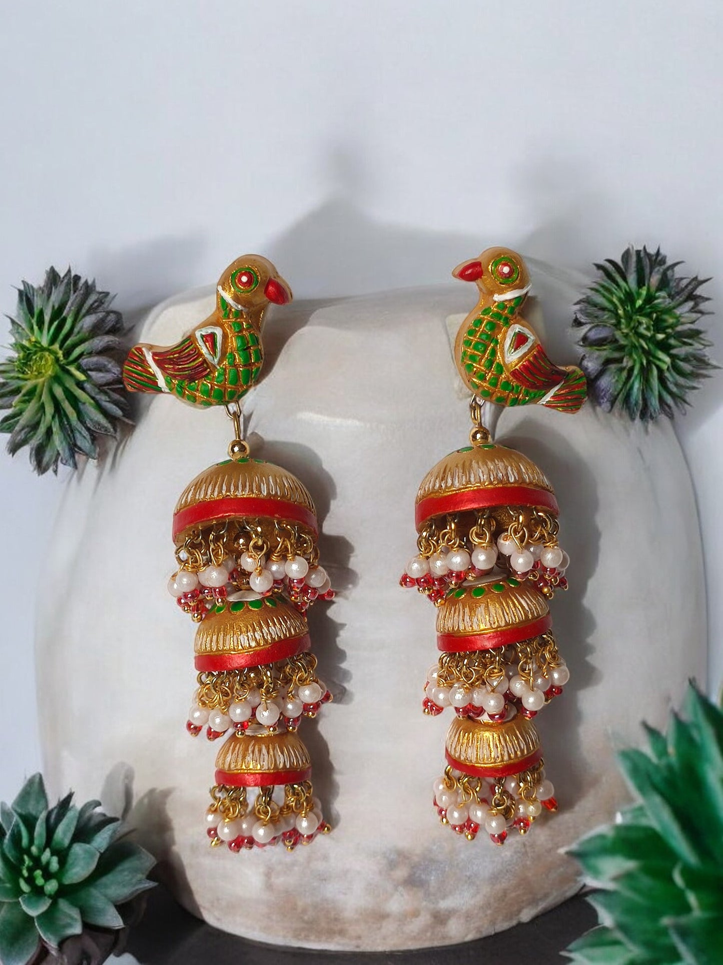 Parrot motif terracotta jhumka earrings with green and red detailing and pearl accents from Anusangi Collections