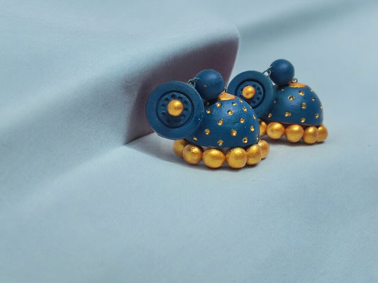 Peacock blue terracotta jhumka earrings with gold accents from Anusangi Collections on light blue fabric