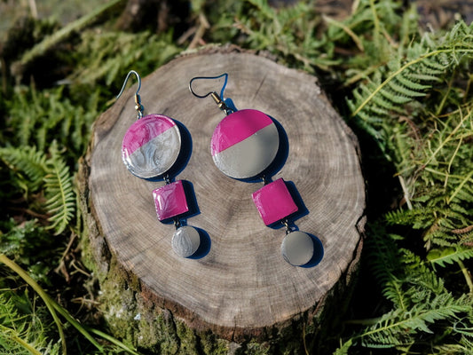Anusangi Collections pink and gray statement earrings made of terracotta displayed on a tree stump