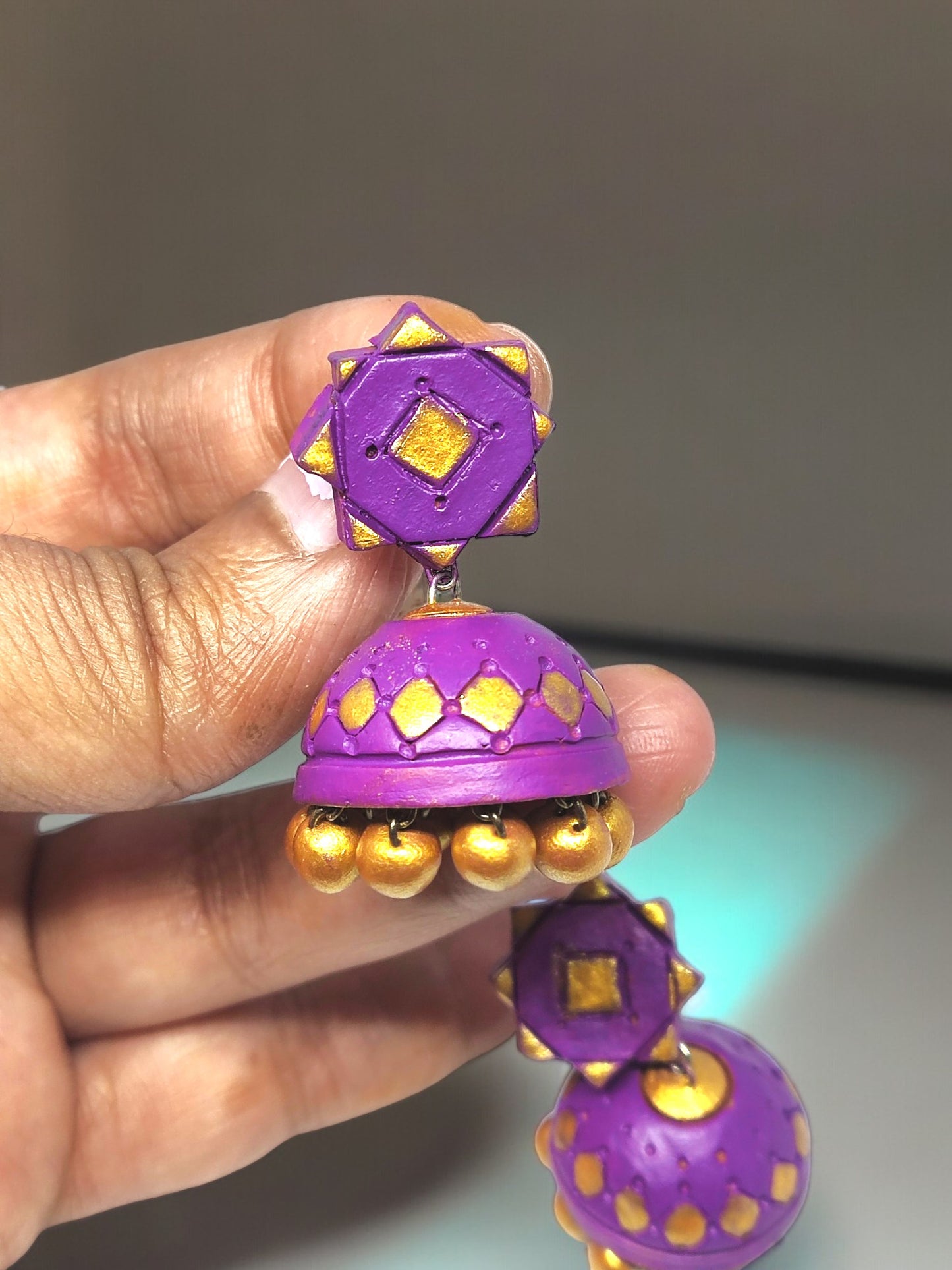 Hand holding purple terracotta earrings with gold accents from Anusangi Collections