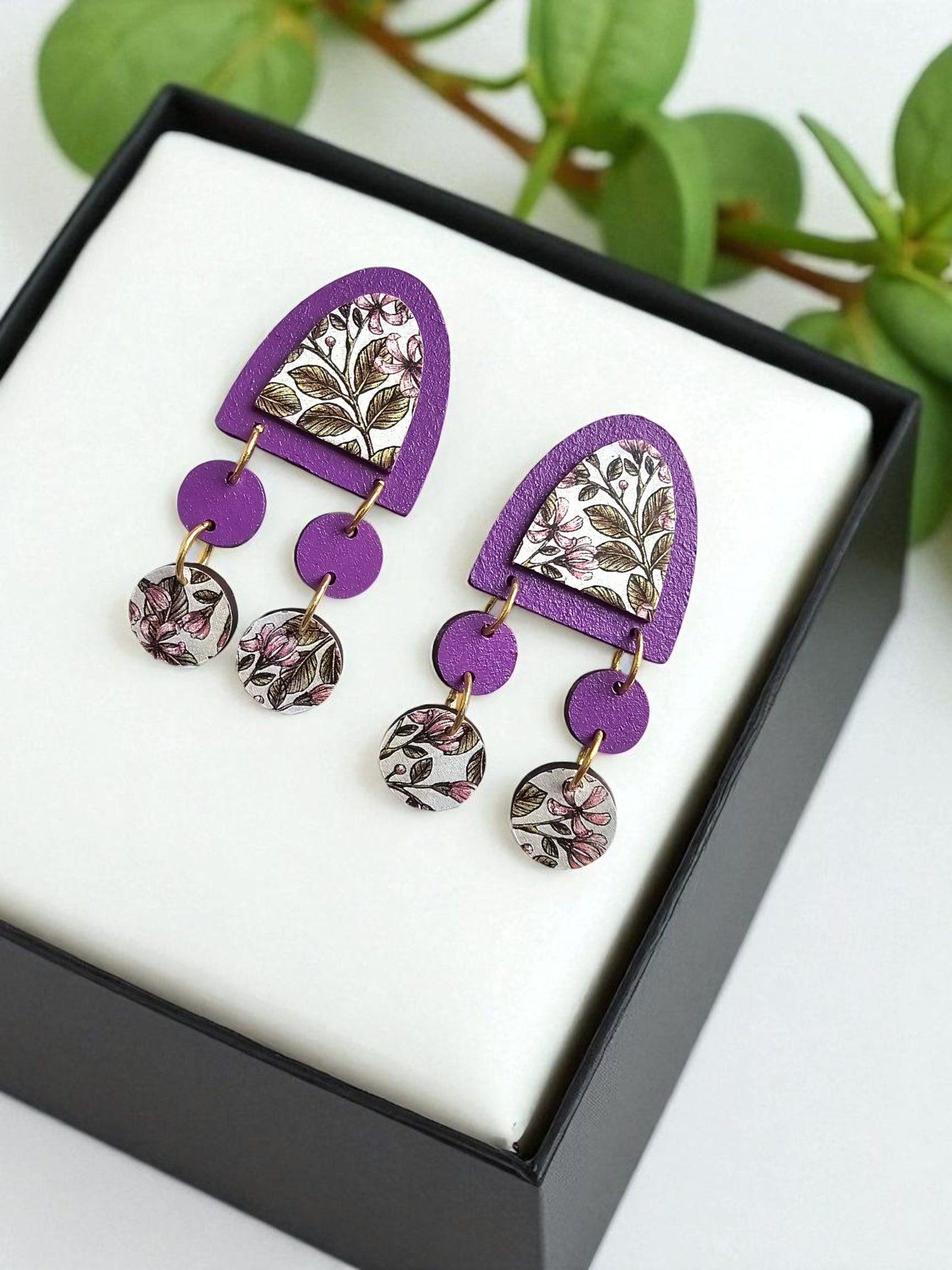 Purple floral earrings in a black box with green leaves in the background