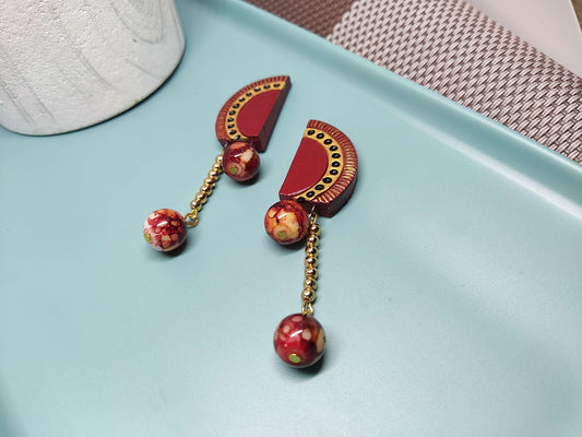 Anusangi Collections statement terracotta earrings featuring red semicircle and hanging bead design on a blue tray