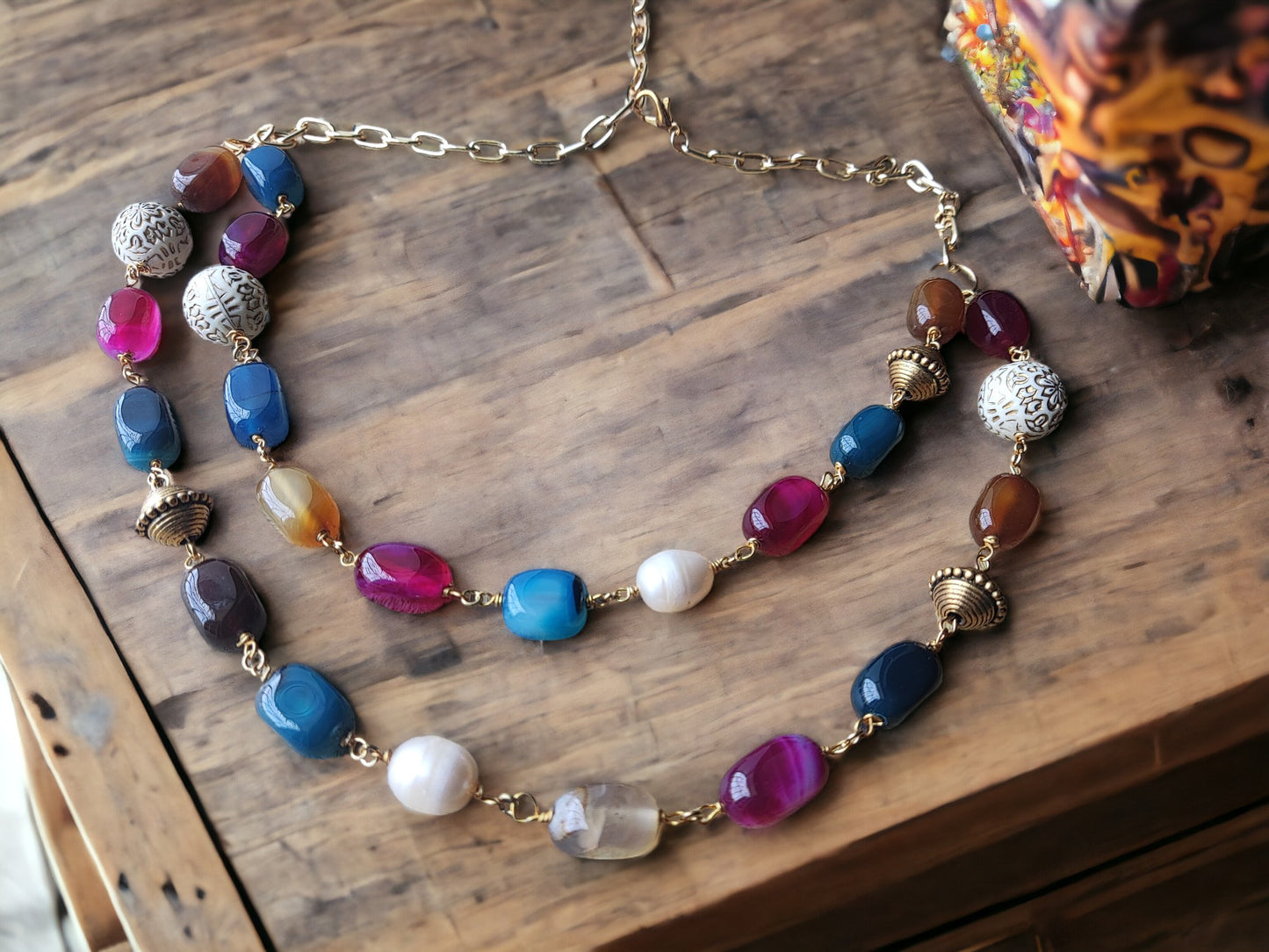 Anusangi Collections double layer handmade necklace featuring colorful beads and metal accents on a wooden surface