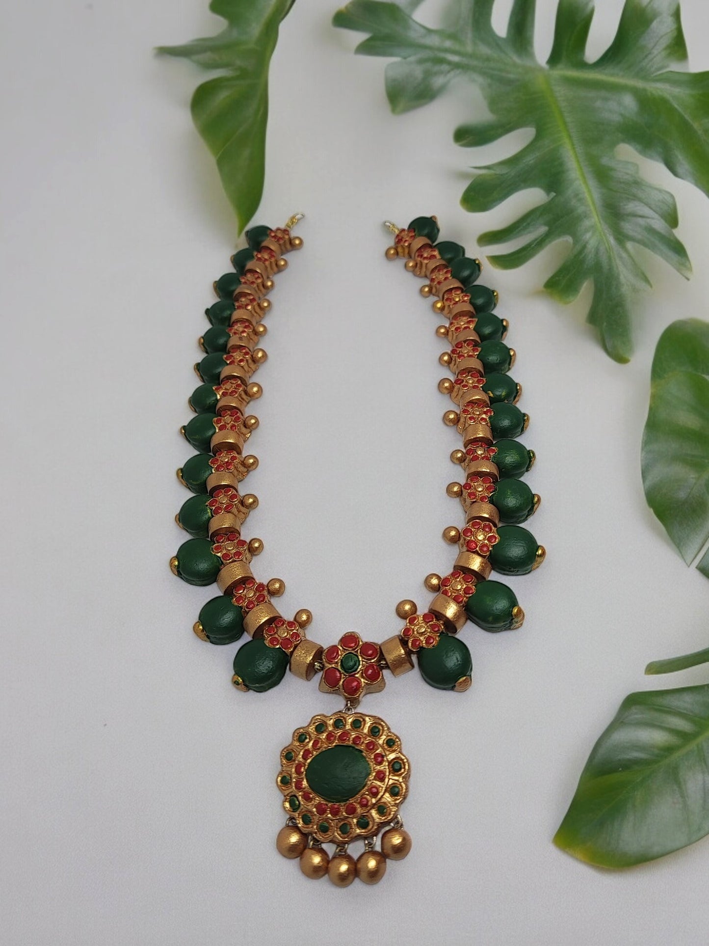 Anusangi Collections grand terracotta necklace and earrings set with green and red detailing on a white background