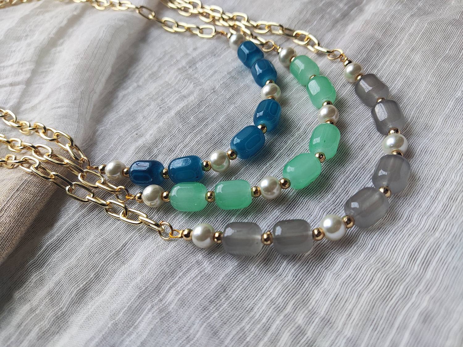 Elegant beaded jewelry set featuring colorful blue green and gray beads with gold chains and pearl accents