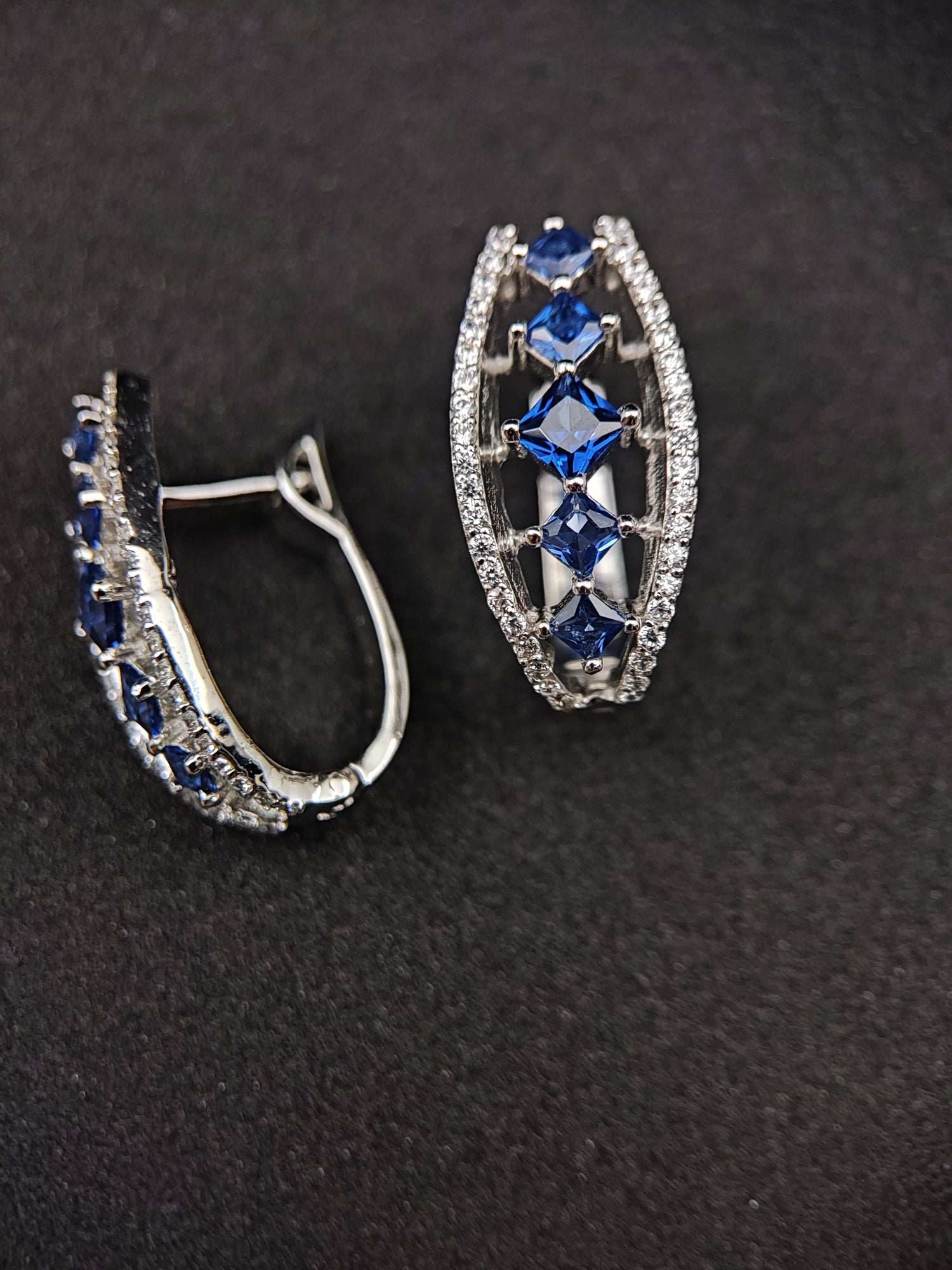 Elegant sterling silver jewelry collections featuring earrings with blue gemstones and clear crystals on black background