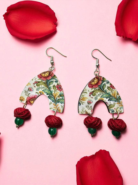 Floral earrings with red and green accents on a pink background with red petals.