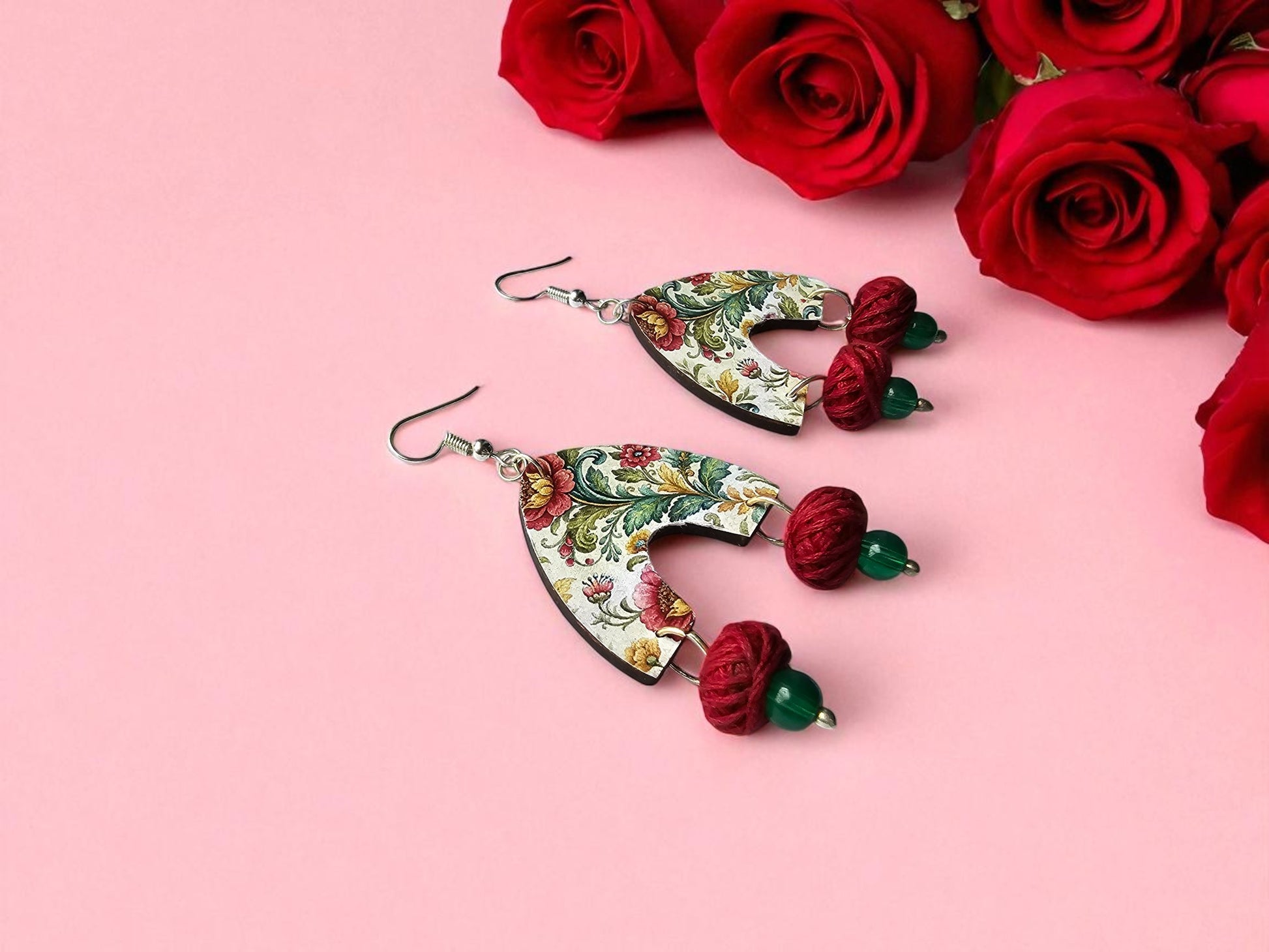 Decorative earrings with floral patterns and red roses on a pink background