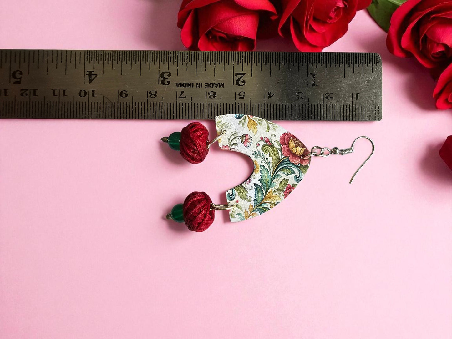 Floral patterned earrings with red floral charms on a pink background with a ruler for scale.