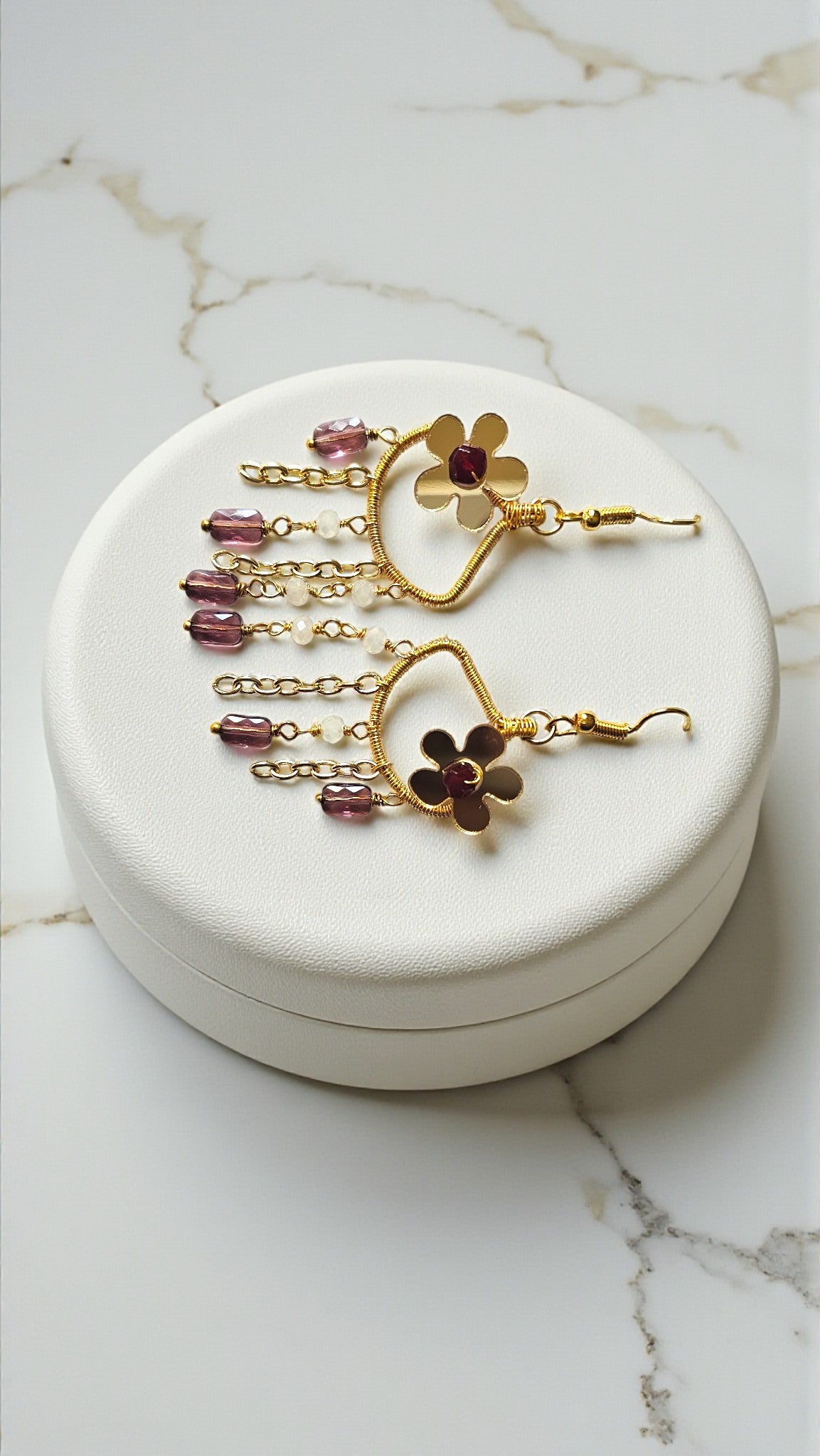 Gold earrings with floral designs and pink gemstones on a white jewelry box.