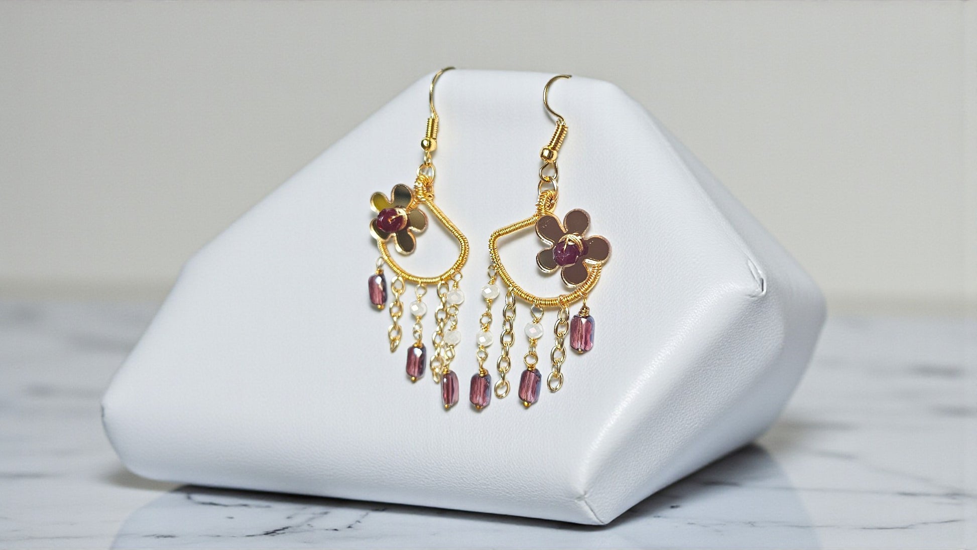 Gold earrings with red gemstones on a white jewelry display stand.