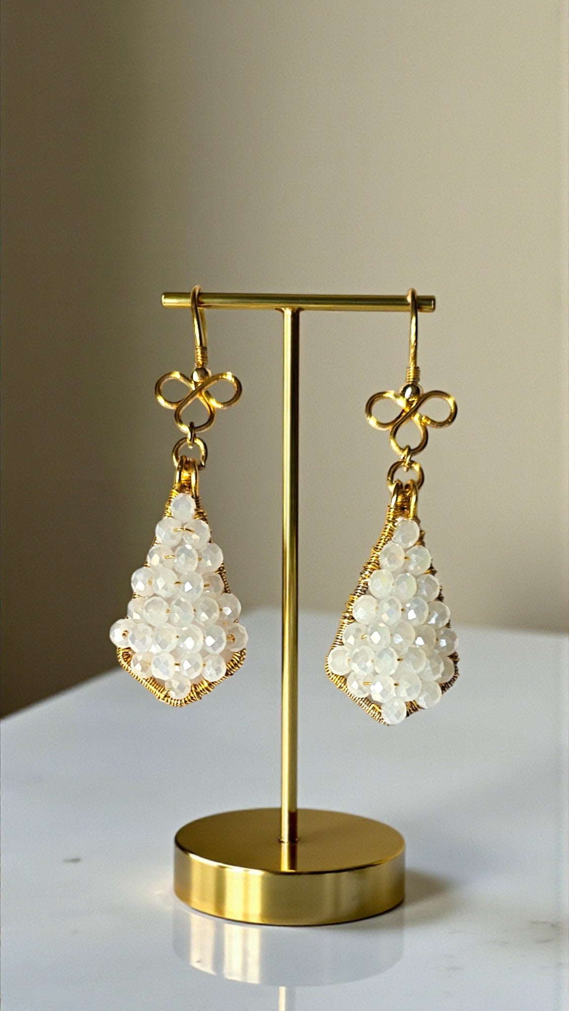 Gold earrings with white beads on a gold stand against a neutral background