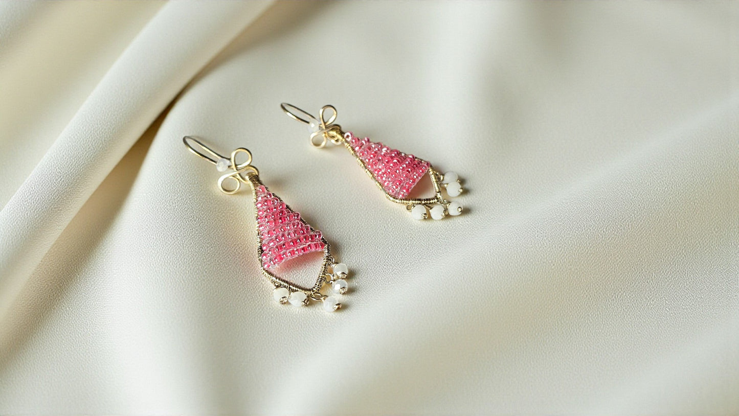 Pink teardrop earrings with gold accents on a beige fabric background