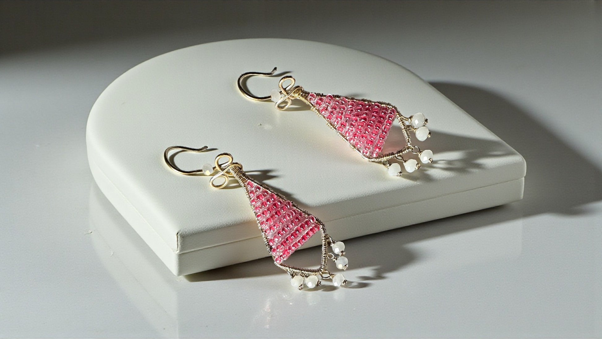 Pink triangle-shaped earrings with gold hooks on a white jewelry box.
