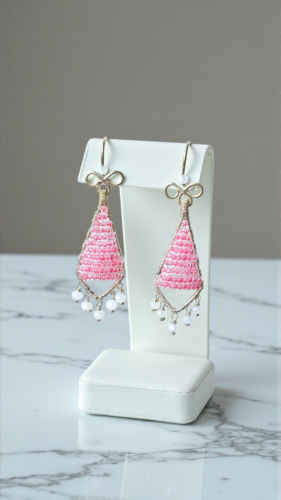 Pink teardrop earrings on a white earring stand with a gray background