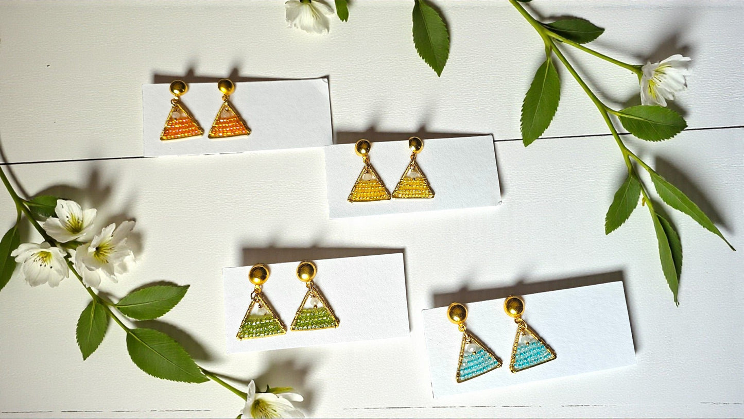 Pair of gold triangle earrings on a white card with green leaves and flowers in the background