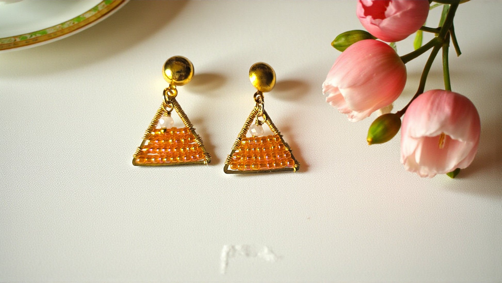 Triangle-shaped earrings on a white surface with pink flowers.