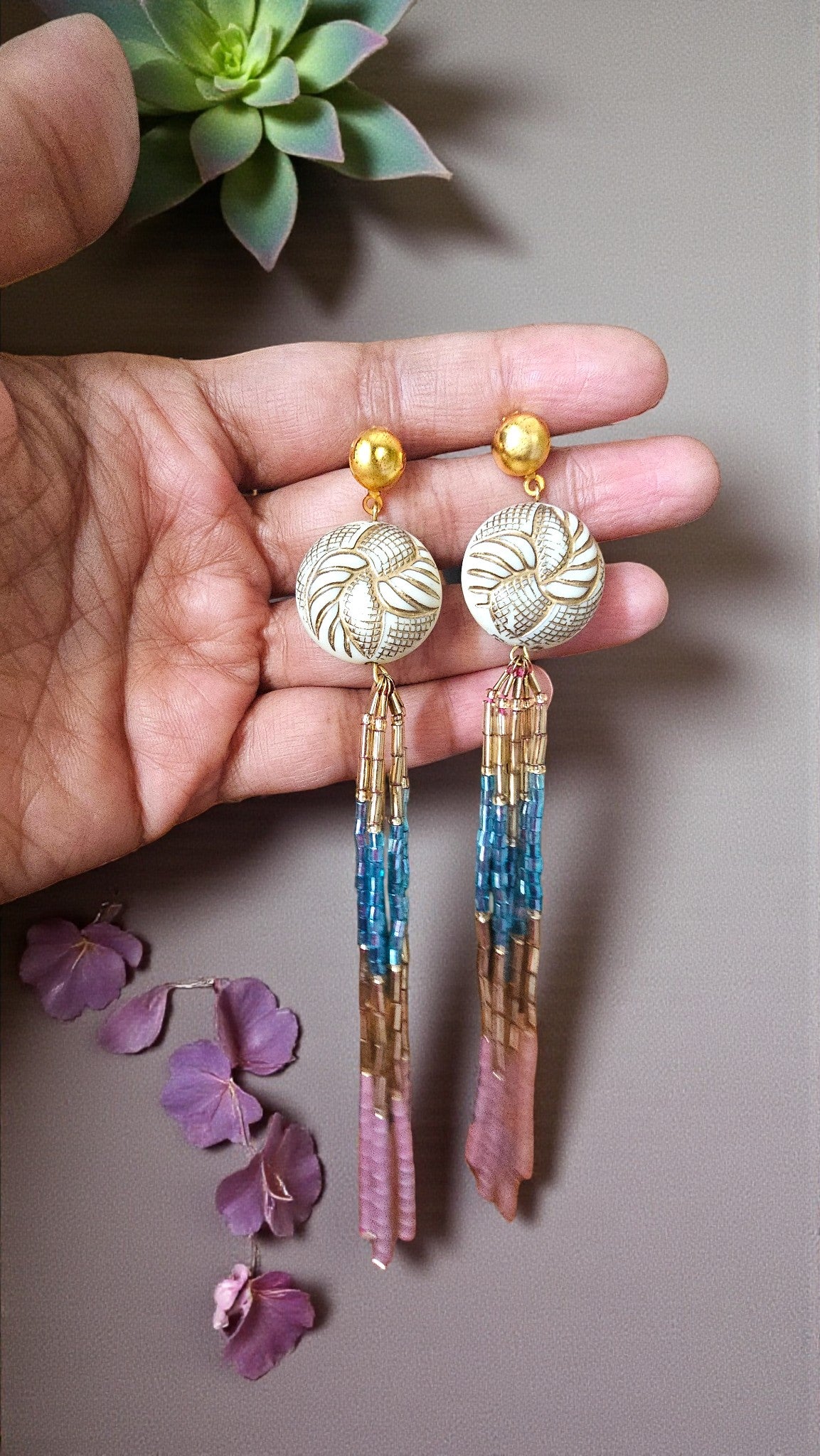 Earrings with decorative elements held by a hand against a neutral background