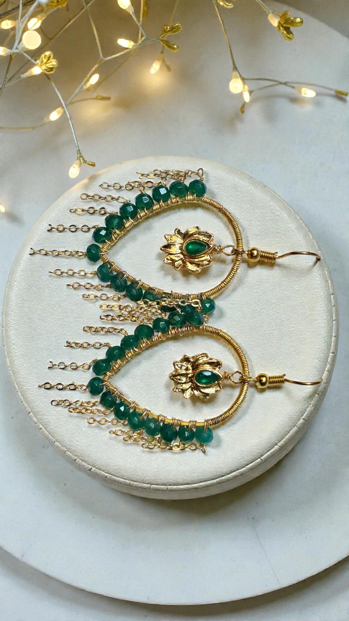 Gold and green jewelry set on a white plate with decorative lights in the background