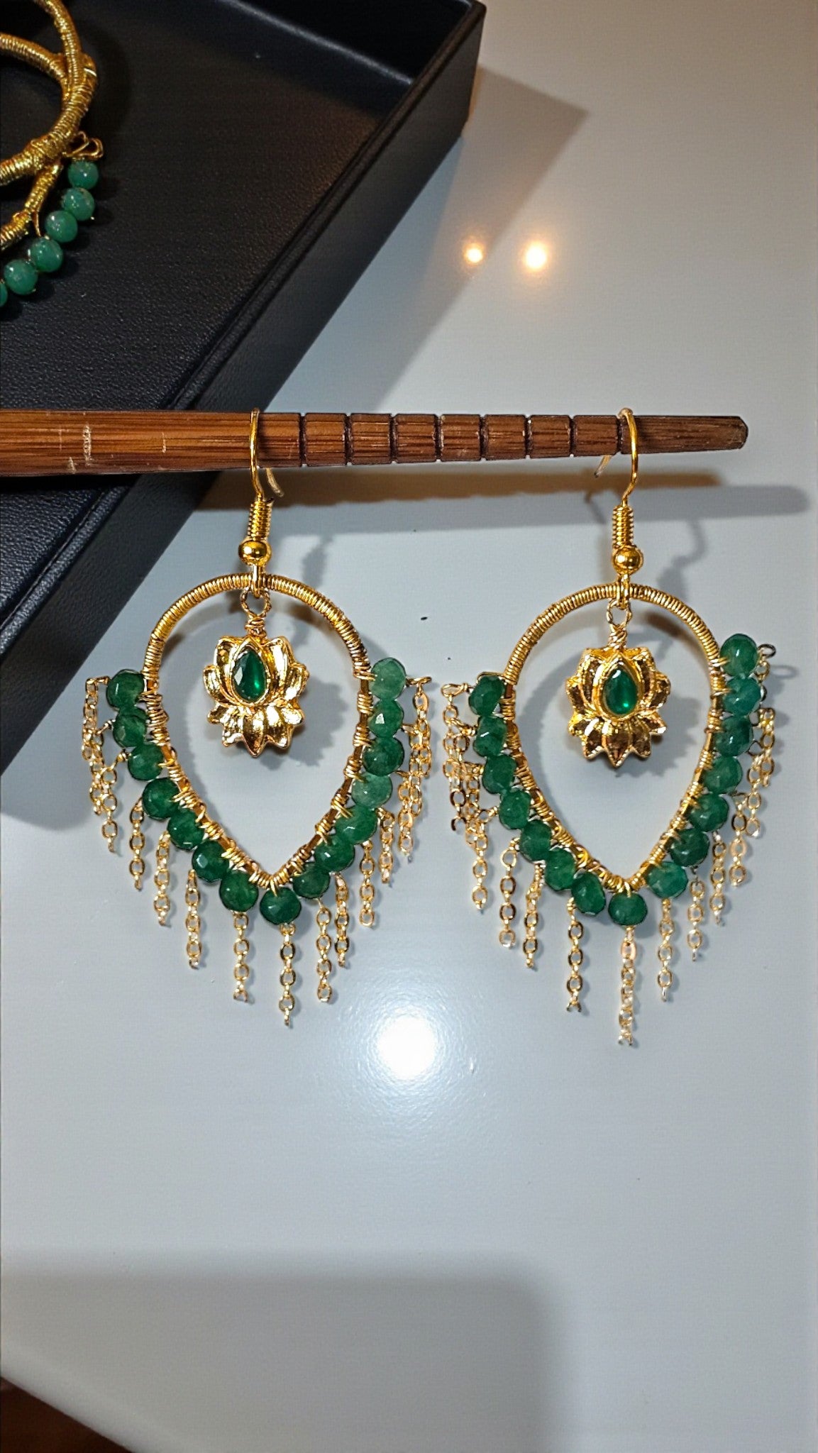 Gold and green earrings on a wooden stand with a white background