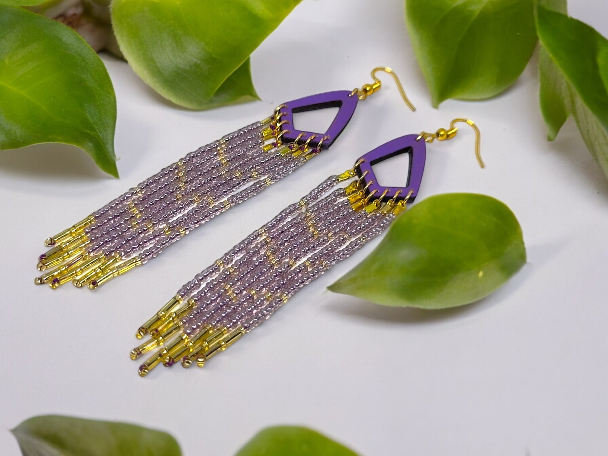 Purple and gold beaded earrings on a white surface with green leaves.