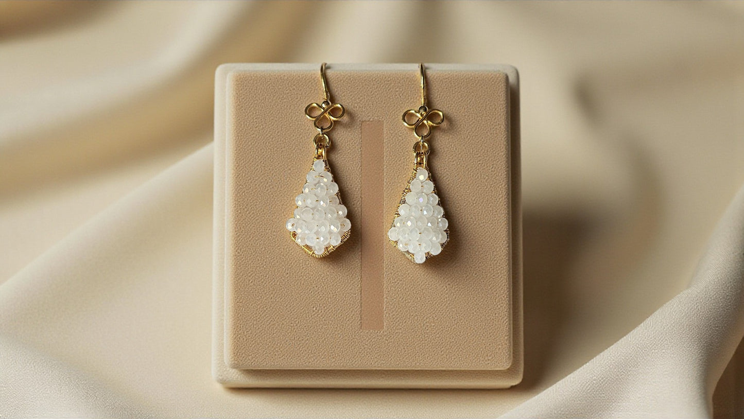 Aahana white bead wrap earrings on a display stand, featuring elegant teardrop shapes