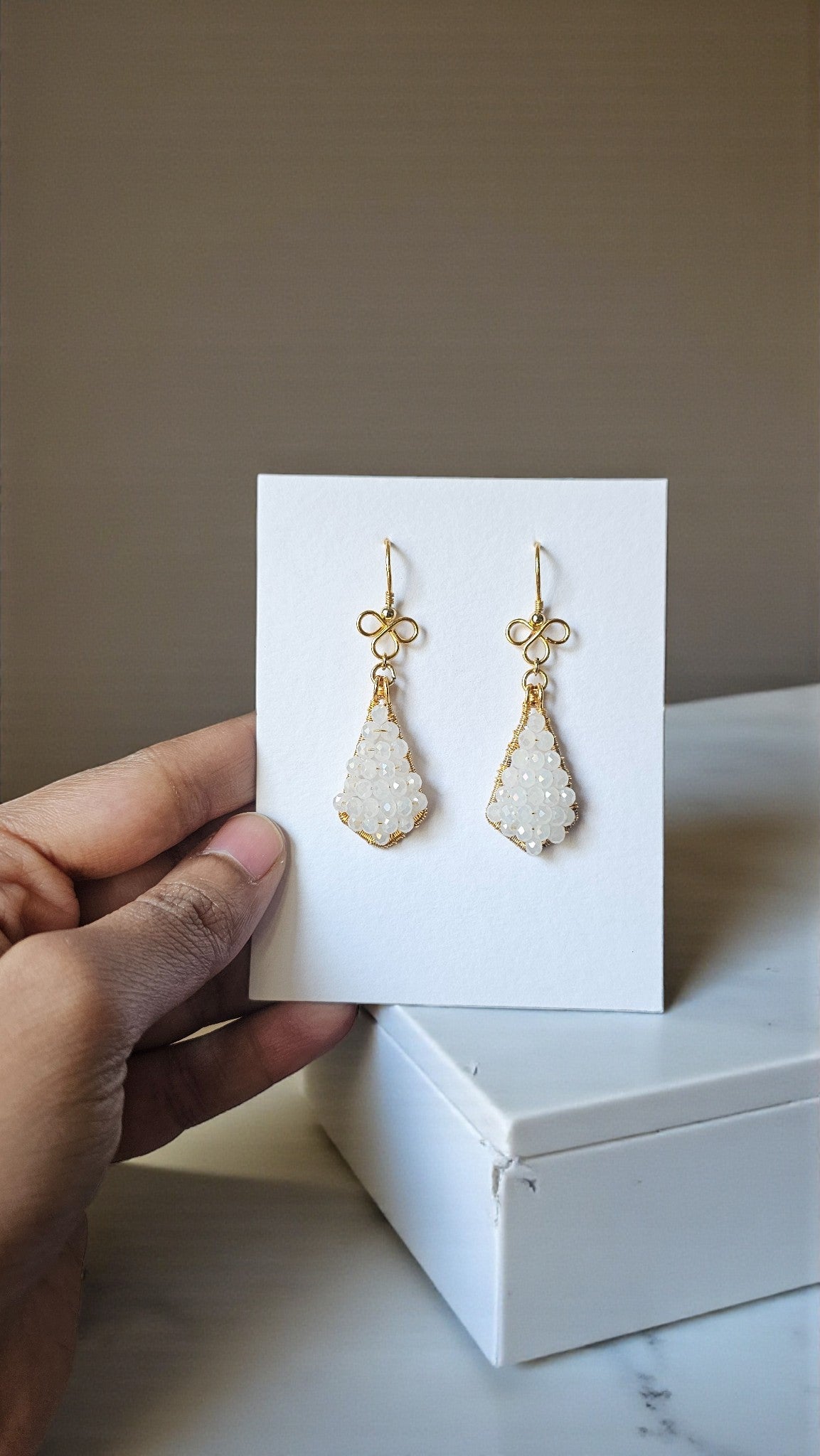 Aahana white bead wrap earrings with gold accents displayed elegantly on a hand