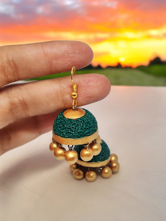 Terracotta ethnic jhumka earrings for women in green and gold held against a sunset background