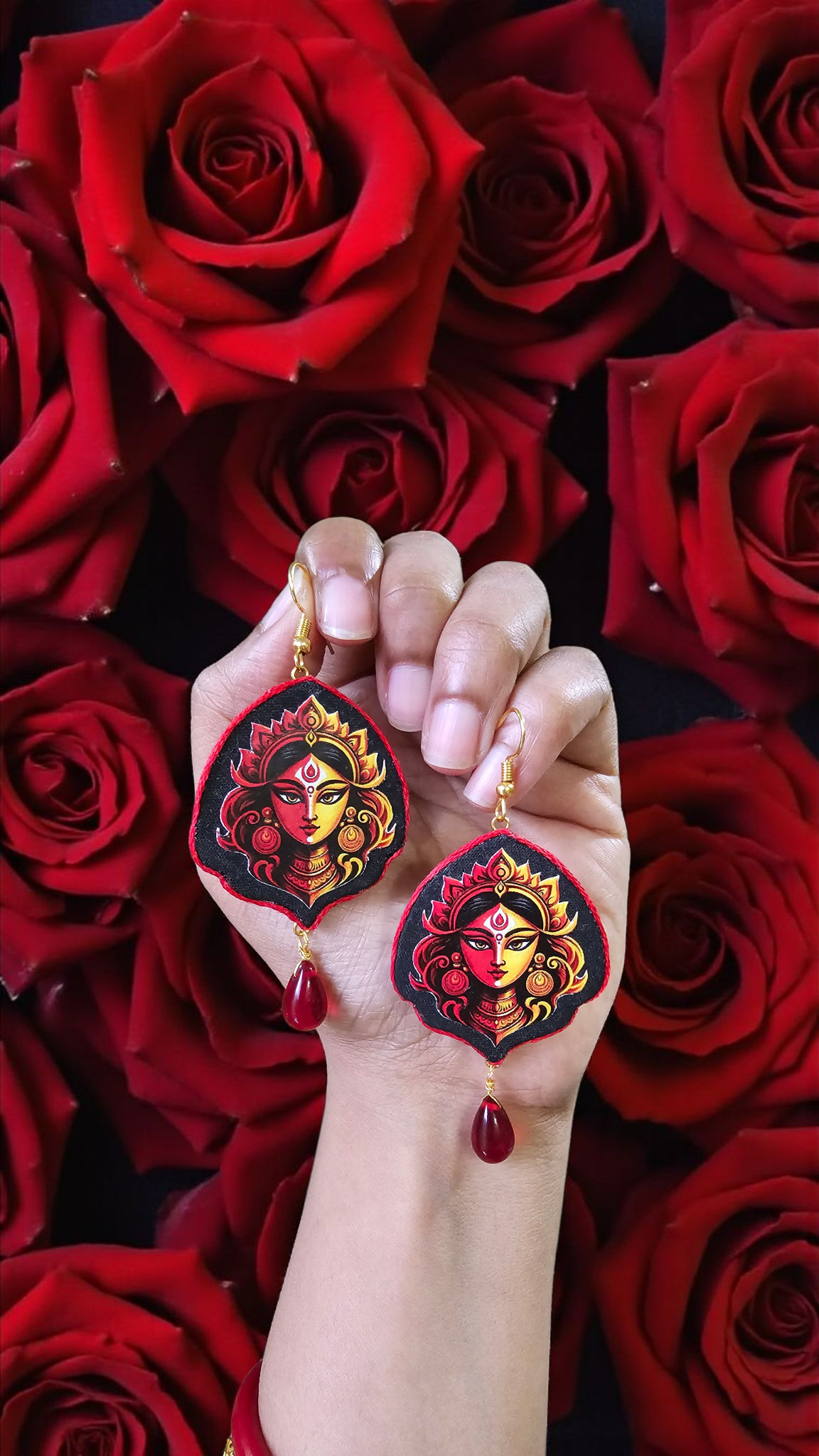 Hand-painted Durga face earrings showcased against a backdrop of red roses