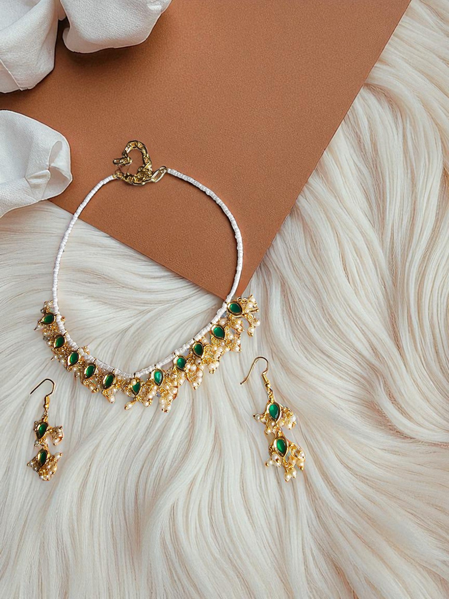 Handmade gold necklace with emerald green beads paired with matching earrings on a textured background