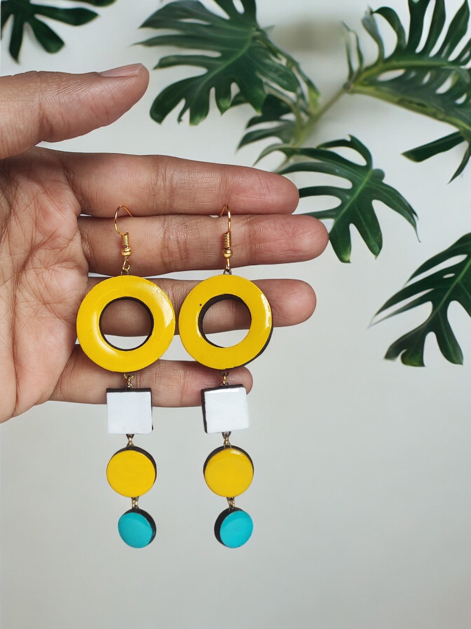 Hand holding colorful handmade terracotta earrings with yellow, white, and blue geometric shapes