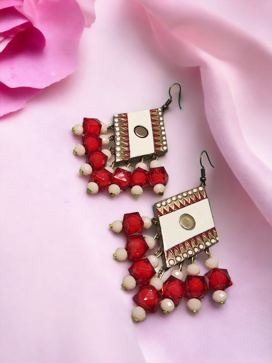 Anusangi Collections red terracotta earrings with white beads and intricate metal detailing on pink fabric