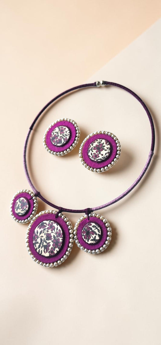 Jewelry set with purple and silver circular designs on a beige background